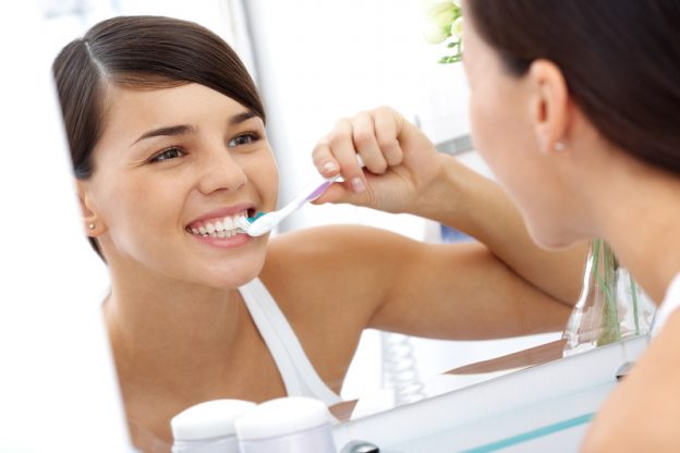 Image of pretty female brushing her teeth in front of mirror in the morning